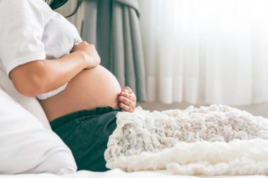 Hamile kadınlar yatakta otururken, anne kavramına dokunmak ve bebeği karnında tutmak için iki elini kullandı..