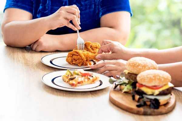 The fat woman sat down to eat together which had fried chicken, pizza and hamburgers, but both fough for the same piece of fried chicken, to food and fat concept.