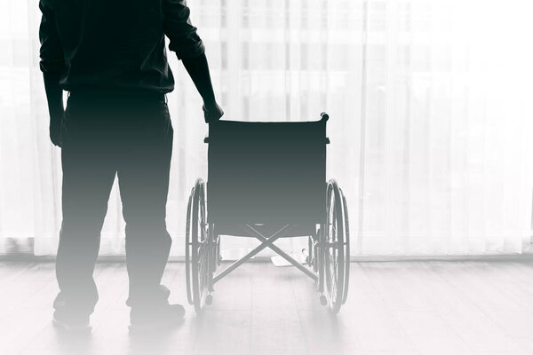Человек, стоящий и инвалидное кресло в больнице с белыми занавесками заднего плана, к концепции здоровья.