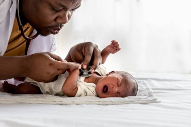 Steteskop kullanan Afrikalı bir doktor, bebek siyah tenli yeni doğan bebek ve sağlık hizmetleri kavramına uzanan ve ağlayan 12 günlük bir bebeğin solunum sistemini ve kalp atışlarını kontrol ediyor..