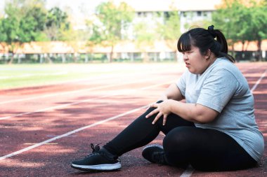 Asian fat woman, is currently having a knee injury During his exercise by running in the running track at the park, due to osteoarthritis, to sports and health care concept. clipart
