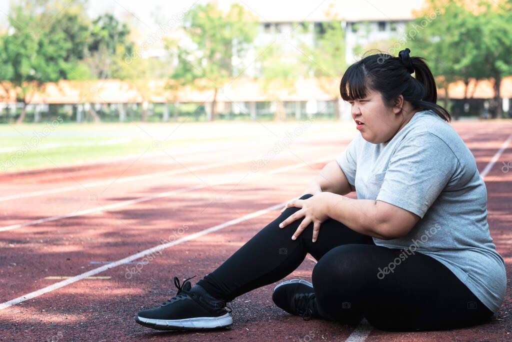 Asian fat woman, is currently having a knee injury During his exercise by running in the running track at the park, due to osteoarthritis, to sports and health care concept.