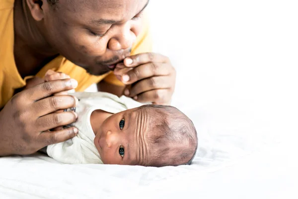 Blurred of An African American father is playing tease with his 12-day-old baby newborn son lying in bed in a white bedroom, with happy, concept to African American family and newborn