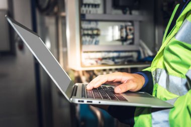 Makinenin endüstriyel fabrikadaki elektrik sistemini kontrol etmek için bilgisayar defteri kullanan mühendis, mühendislik ve endüstri kavramına.