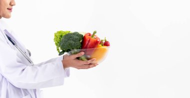 Asyalı kadın doktor, beslenme uzmanı elinde bir kase dolusu taze sebze ve C vitamini olan meyve tutuyor, vücuda yararlı, beyaz arka planda Haealth bakımı ve temiz gıda konsepti..