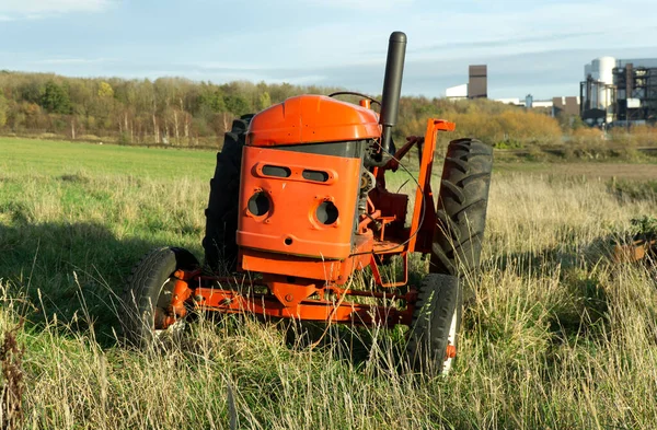 Sad looking red tractor abandoned in a field