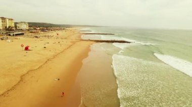 Kayalık rıhtımlı okyanus manzarası ve tanınmayan insanlarla dolu kumlu plaj. Costa Da Caparica