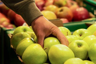 Erkek eli süpermarketteki kutudan yeşil bir elma alır. Marketten elma almak. Elma seçiliyor.