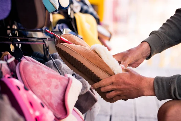 Man choosing warm brown home slippers in the shop. Buying slippers for winter. How to choose comfortable slippers for home. High quality photo