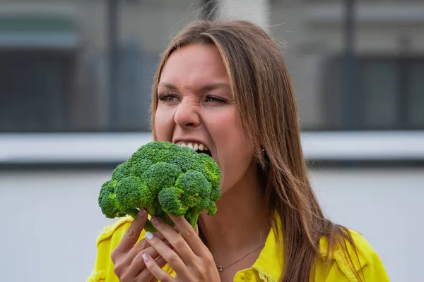 Funny hungry young vegan woman biting broccoli. Lady loves broccoli. Healthy plant based eating concept. Vegetarian, vegan, raw concept — Foto de Stock