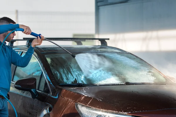 Self serve car washing. Man cleaning car using high pressure water at car washing station.