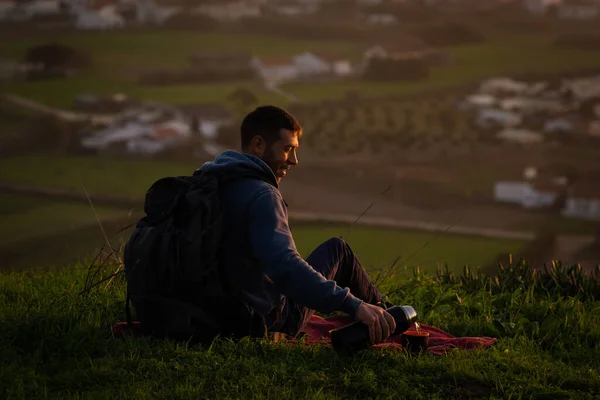 Caminhante homem sentado no chão em montanhas e derramando chá de garrafa térmica para xícara — Fotografia de Stock