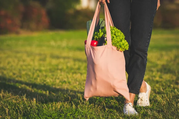 Young woman holding eco reusable textile grocery bag with fresh bio vegetables. Plant based vegan diet shopping. Healthy clean eating. Zero waste, plastic free concept with copy space.