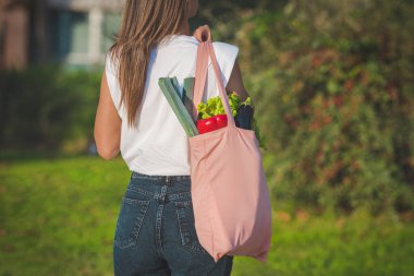 Yeniden kullanılabilen pembe ekolojik çanta ve taze biyo-sebzeli genç bir kadın. Bitki temelli vegan diyeti. Sağlıklı detoks temiz alışveriş. Sıfır atık, plastiksiz konsept
