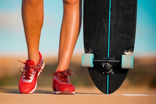 Sportieve vrouw met een skateboard of longboard op een zonnige zomerdag. Close-up op schoenen — Stockfoto