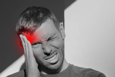 Young man touching his temple and having strong tension headache. Cluster headache. Man suffering from migraine, stress, hangover with red alert accent. Hands on head. High quality photo clipart