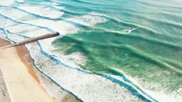 Воздушный вид на океанские волны ломается на песчаном пляже. Скалистый пирс или волнолом в океане. Costa Da Caparica, Portugal — стоковое видео