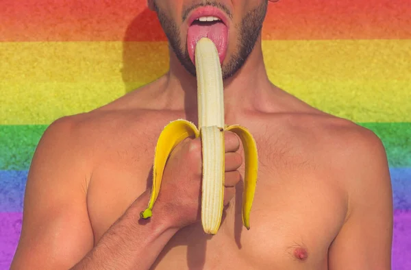 若い男の半分を食べて、黄色のバナナの皮をむいたルブト虹の背景に。レズビアン、ゲイ、バイセクシャル、トランスジェンダーのコミュニティの権利支援. — ストック写真