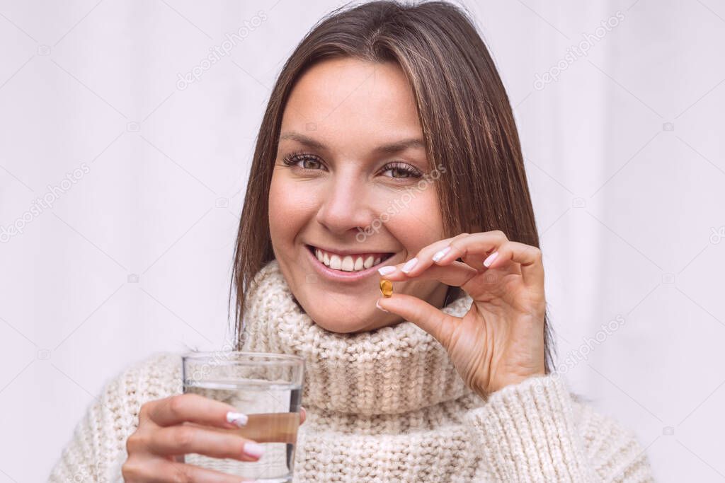 Vitamins and food supplements. Close up of happy smiling woman holding a glass of water and taking a pill with cod liver oil omega-3. Vitamin D, D3, fish oil capsules. Healthy diet nutrition concept