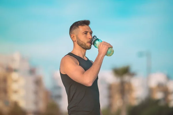 Giovane fitness uomo bere acqua dalla bottiglia riutilizzabile durante un allenamento. Bere mentre ti alleni. Disidratazione durante l'esercizio — Foto Stock