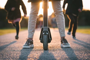 Gün batımında yolda elektrikli scooterlı genç bir kadına yaklaş.