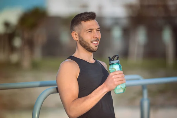 Giovane fitness uomo bere acqua con limone da bottiglia riutilizzabile durante un allenamento. Bere mentre ti alleni. Disidratazione durante l'allenamento — Foto Stock