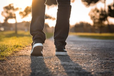 Man walking outdoors in the park at sunset. Closeup on shoe, taking a step.  clipart