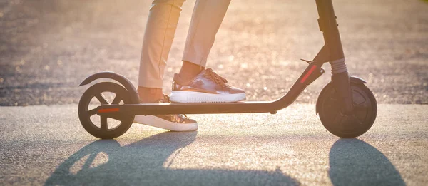 Primo piano di donna elegante guida scooter elettrico calcio al tramonto. Trasporto elettrico ecologico — Foto Stock