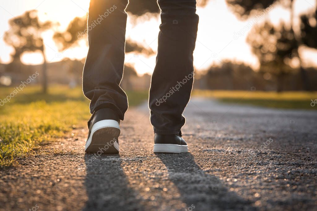 Man walking outdoors in the park at sunset. Closeup on shoe, taking a step. 