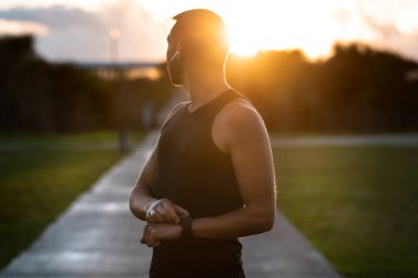Genç, sağlıklı atletik bir adam gün batımında spor takip cihazı ya da akıllı yamakla koşuyor. Eğitim sırasında kablosuz kulaklıkla müzik dinlemek. Aktif yaşam tarzı ve teknoloji