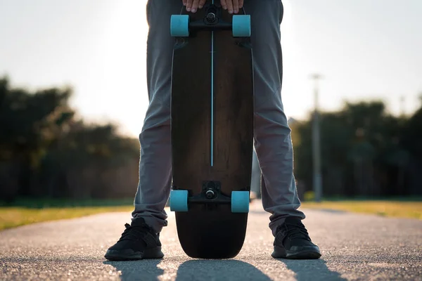 Чоловік тримає чорний скейтборд на відкритому повітрі на заході сонця — стокове фото