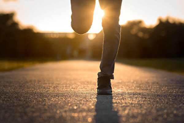 Close up of man legs running at sunset. Man running jogging on city park road