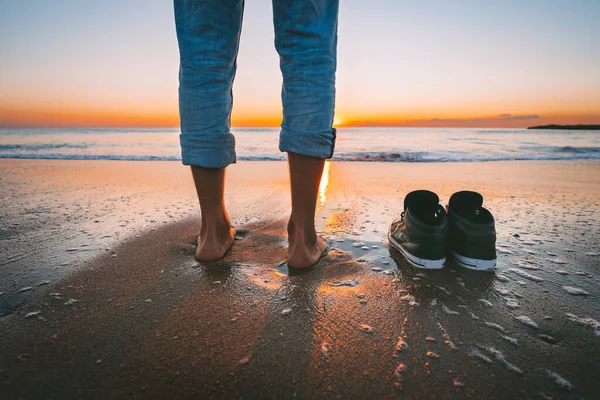 Penutup dari pria bertelanjang kaki berjalan di pantai musim panas saat matahari terbenam. Orang melepas sepatunya untuk berjalan di laut yang tenang. Konsep relaksasi dan kebebasan. — Stok Foto