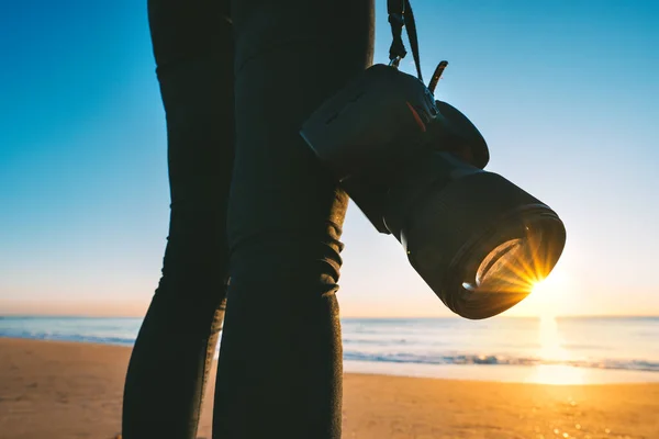 Close-up van vrouwelijke fotografe met haar professionele camera op het strand bij zonsondergang. Zonsondergang fotografie — Stockfoto