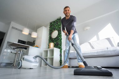Evde elektrikli süpürge kullanan çekici bir genç. Adam evi temizliyor. Ev tutma kavramı