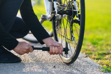 Parkta bisiklet tekerleği pompalayan bir adam. Adam pompa kullanarak bisiklet tekerleğini şişiriyor. Boş bir bisiklet tekerleğine hava pompalamak.