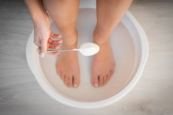 Mujer puso cuchara de bicarbonato de sodio en el baño con agua caliente para sus pies. Remojo casero del baño para la piel seca de los pies. — Foto de Stock