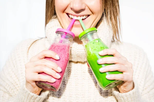 Wanita dengan sweater wol memegang 2 botol smoothie detox merah muda dan hijau buatan sendiri atau jus. Detoks sehat memakan makanan yang bersih — Stok Foto