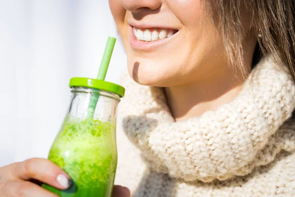 Wanita tersenyum dengan sweater wol meminum detox smoothie atau jus buatan sendiri berwarna hijau. Makanan sehat yang bersih — Stok Foto