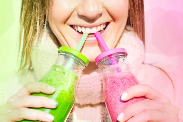 Senyum wanita minum dari 2 botol dengan smoothie merah muda dan hijau buatan sendiri — Stok Foto