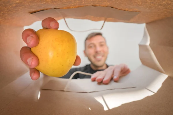 Счастливчик, берущий яблоко из бумажного пакета. Доставка на дом из продуктового магазина во время самостоятельного карантина, КОВИД-19. — стоковое фото