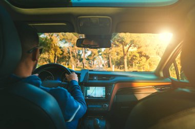 Gün batımında araba süren genç bir adam. Araba kullanırken navigasyon sistemi kullanan bir adam