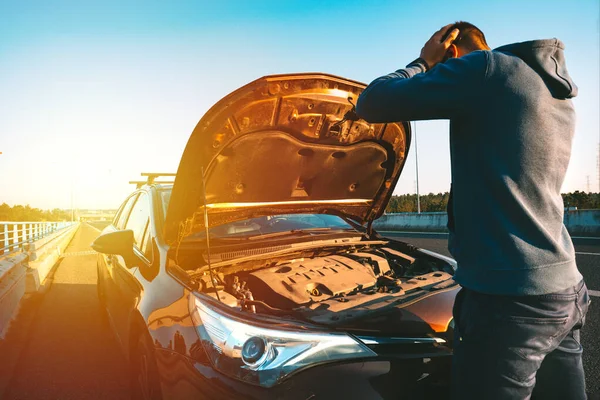 Stressad man har problem med sin trasiga bil på motorvägen vid solnedgången. Mannen som tittar under motorhuven. Bilen går sönder på autobahn. Begreppet vägassistans. — Stockfoto