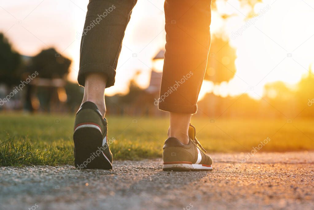 Woman walking in the park at sunset. Closeup on shoe with rolled up jeans. Taking a step. Woman on his way to a new better life. The way forward. New start, new life and freedom concept. 