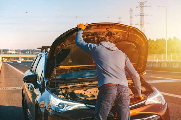 Een man die problemen heeft met zijn kapotte auto langs de snelweg. Een man die onder de motorkap kijkt. Auto begeeft het op de autobaan. Begrip "technische bijstand". — Stockfoto