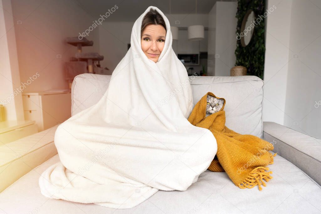 Woman feeling cold. Woman and cat warming under a blanket on the sofa at home. Freezing from cold 