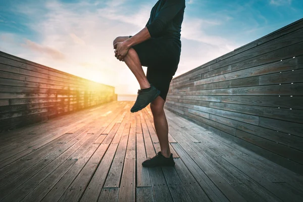 Sportif adam gün batımında ya da gün doğumunda dışarıda antrenmandan önce ısınıp bacaklarını esnetiyor. Gluteus maximus kas esnetiyorum. Sporcu adam spor yapıyor, esneme egzersizleri yapıyor. Spor ve sağlıklı yaşam tarzı — Stok fotoğraf