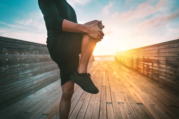 Fitness adamı gün batımında ya da gün doğumunda dışarıda antrenmandan önce ısınıyor ve bacaklarını esnetiyor. Spor ve sağlıklı yaşam tarzı — Stok fotoğraf