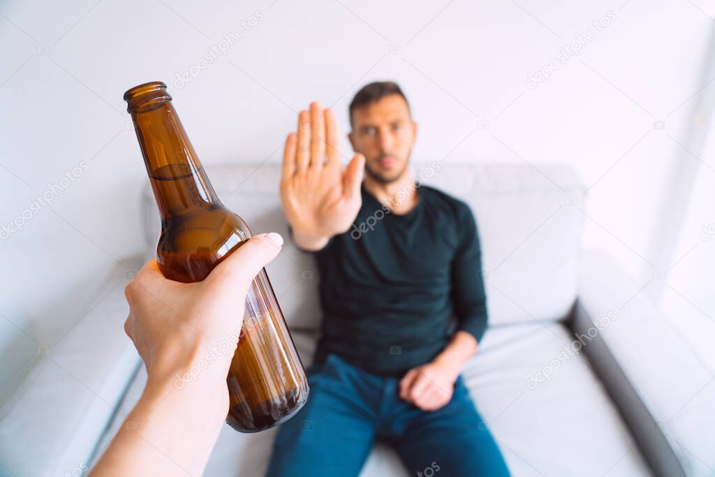 No alcohol. Young man refuses to drink beer, making stop gesture to bottle of beer