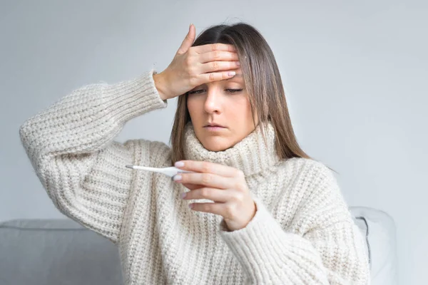 Sick unhealthy woman with fever measuring temperature with a medical thermometer